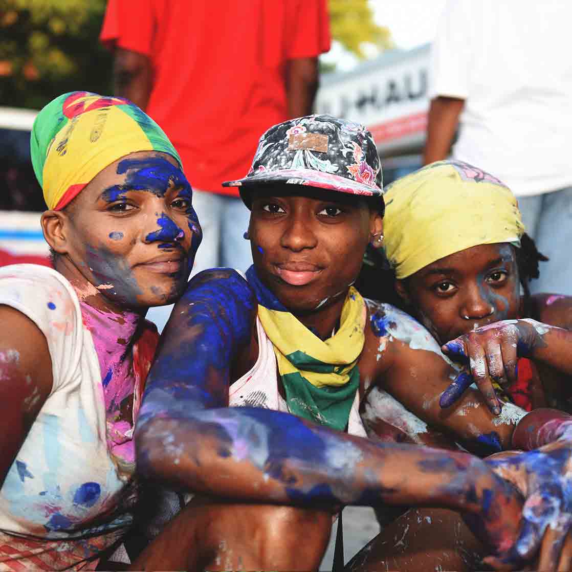 3 Grenadian children with colouring on their face sitting